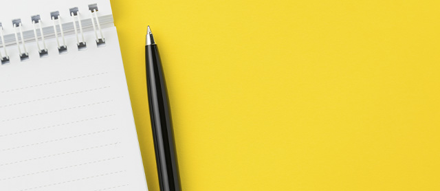 caneta esferográfica ao lado de um caderno em um fundo amarelo