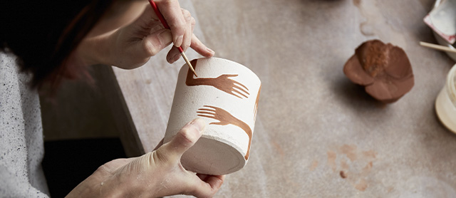 mulher usando um pincel fino para pintar um vaso de cerâmica