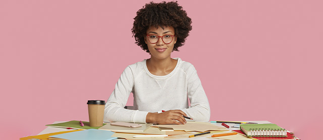 garota sentada em uma escrivaninha organizando as anotações de seu caderno de estudos