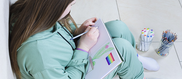 garota sentada no chão desenhando em um caderno de desenho com materiais de papelaria criativa