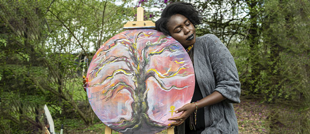 mulher abraçada com um quadro que pintou como forma de autoexpressão