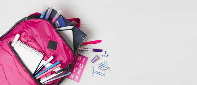 mochila escolar aberta em cima de uma mesa com materiais artísticos saindo dela